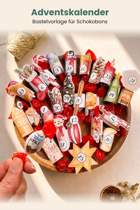 Hand hält einen Schokobon über einer Holzschale mit 24 beklebten Banderolen, Adventskalender zum Ausdrucken
